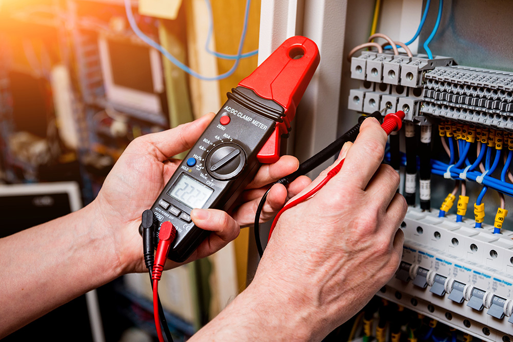 Omaha Home, Kitchen, Bathroom and Basement Remodeling - A technician uses a multimeter to measure voltage in an electrical panel, focusing closely on the task with various wires and connections visible.