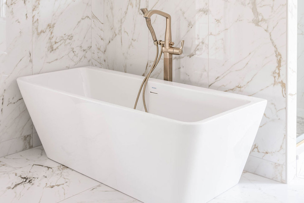 Omaha Home, Kitchen, Bathroom and Basement Remodeling - Modern home interior featuring a sleek kitchen island with a white countertop and dark cabinet, complemented by light gray tiled flooring leading to an elegant staircase with a white railing.