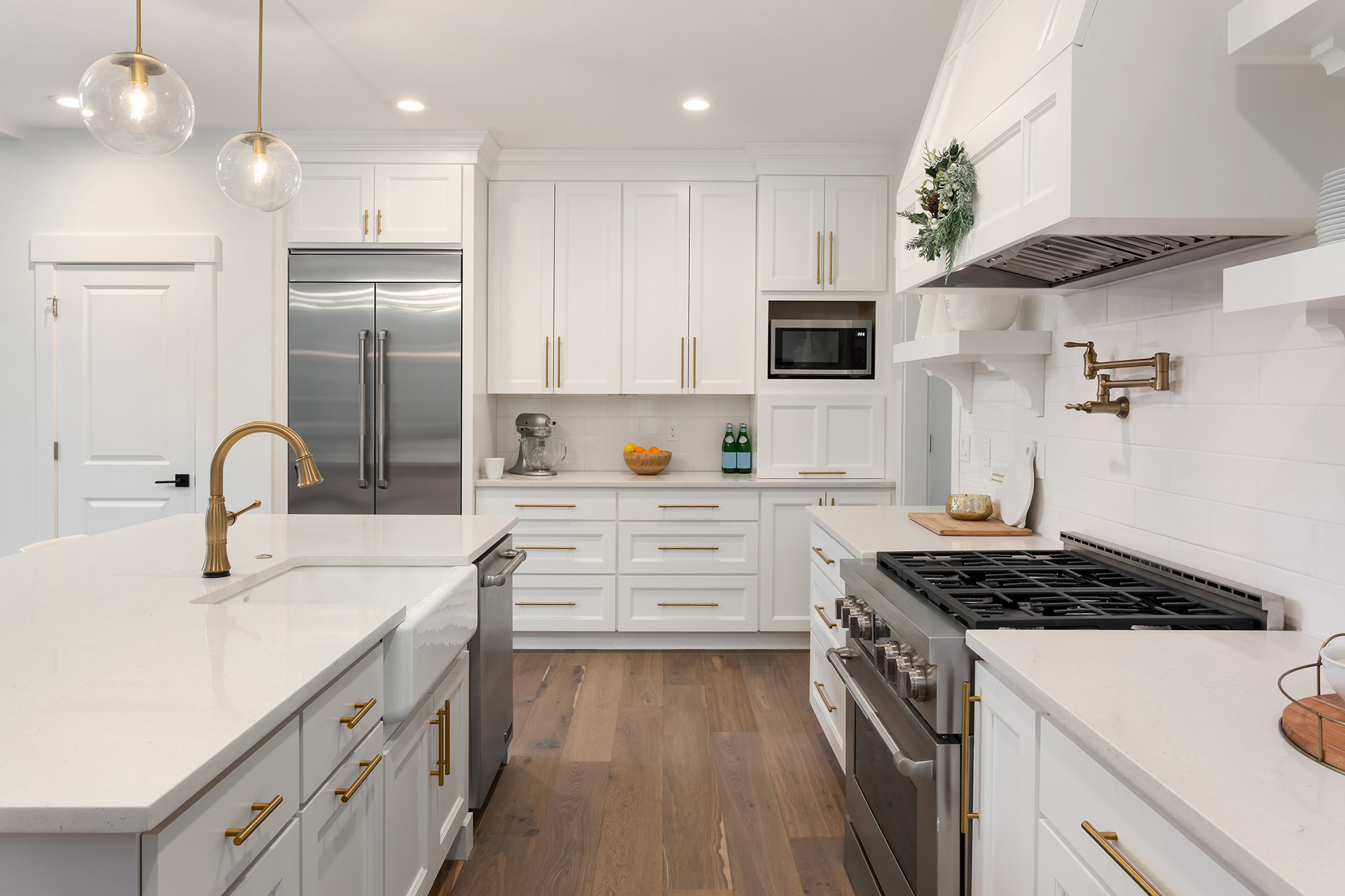 Omaha Home, Kitchen, Bathroom and Basement Remodeling - A modern kitchen featuring white cabinetry, stainless steel appliances, gold accents, and a large center island with a white countertop.